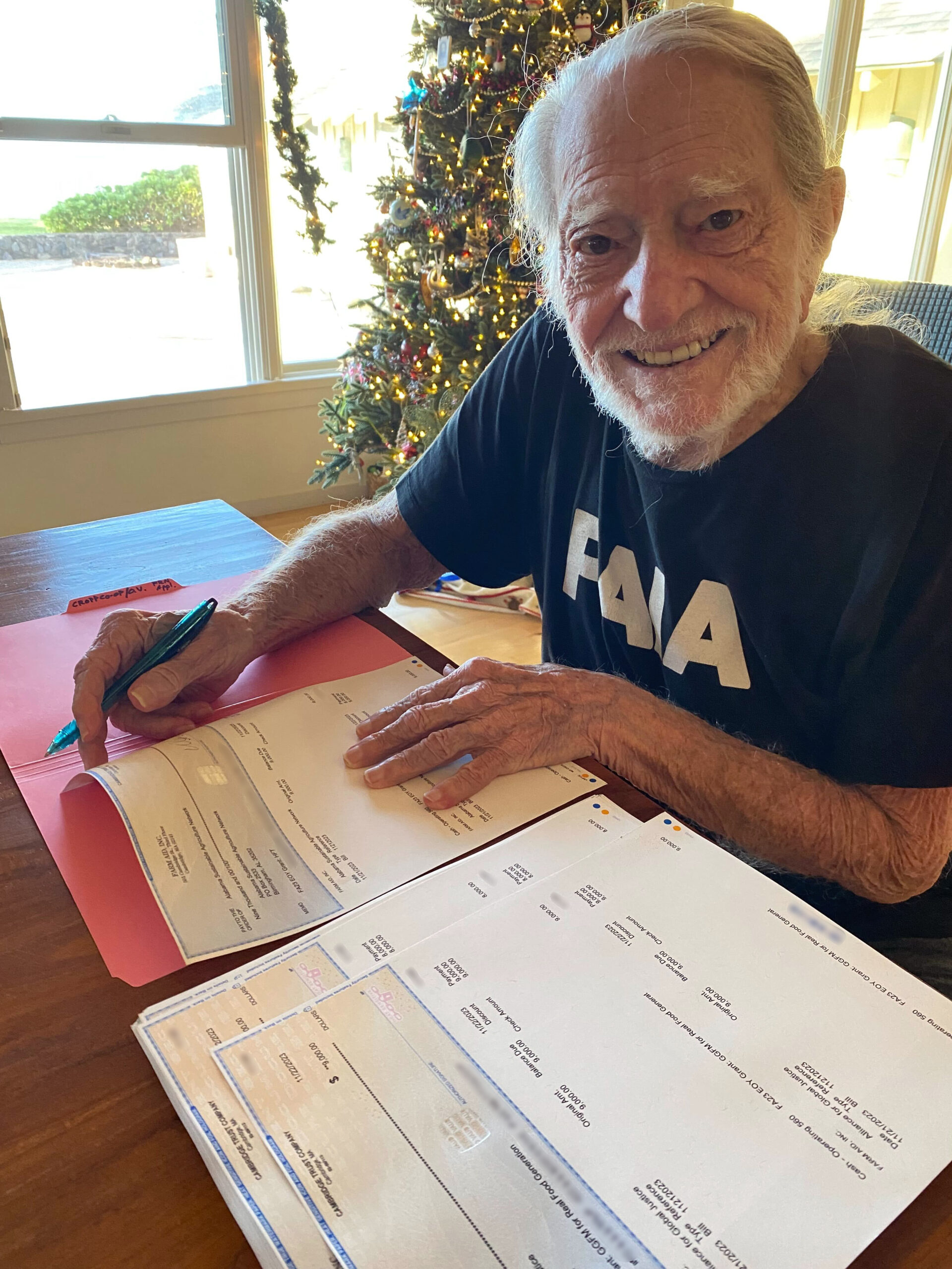 https://www.farmaid.org/wp-content/uploads/2023/12/willie_nelson_signing_2023_grant_checks_blurred-vertical-scaled.jpg