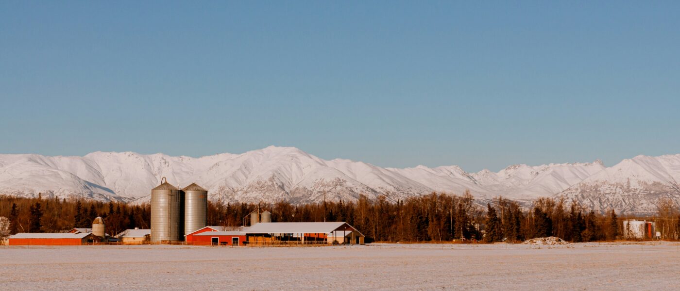 snowy farm scene in front of snowy mountains