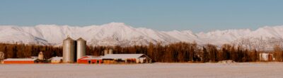 snowy farm scene in front of snowy mountains